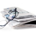 reading glasses resting on the side of a closed newspaper