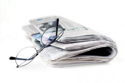 pair of reading glasses resting on a closed newspaper - white background