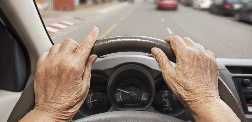 POV close up of an older driver with their hands on the wheel, looking out the windshield at the road