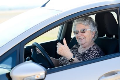 older female driver wearing sunglasses and giving thumbs up