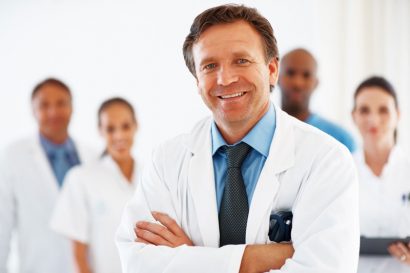 smiling male doctor in white lab coat smiling with a team of doctors behind him