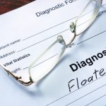 reading glasses sitting on top of a worksheet showing a diagnosis of eye floaters