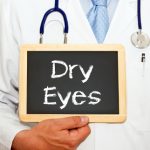 male doctor in a white lab coat holding a chalkboard with dry eyes written on it