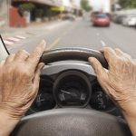 POV of an older female driver with her hands on the steering wheel staring through the windshield