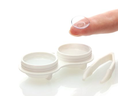 close up of an open contact lens case and a finger holding a contact lens on its tip