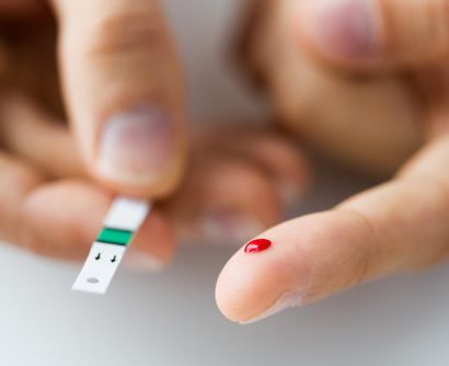 close up of a male finger with a spot of blood and a blood sugar level testing strip