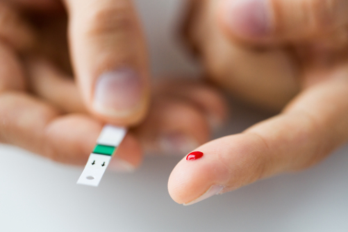 spec of blood on a male fingertip with a blood sugar level test strip for diabetes