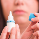 close up of a woman with the cap off a bottle of eye drops readying for application