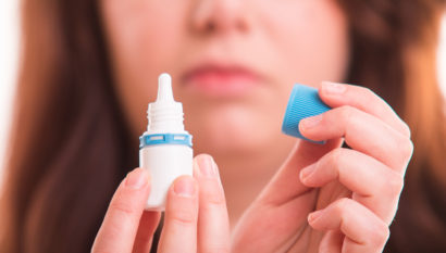 close up of a woman with the cap off a bottle of eye drops readying for application