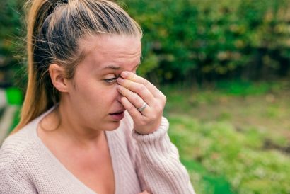 woman outdoors rubbing eyes allergies