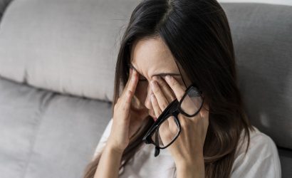 tired woman with glasses rubbing her eyes on sofa