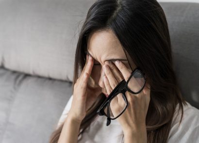 tired woman with glasses rubbing her eyes on sofa